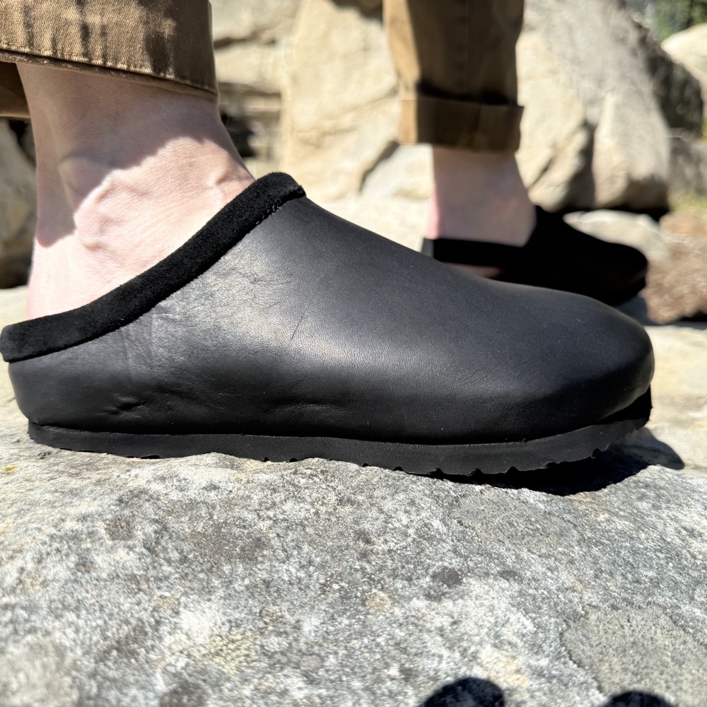 Side profile of a slip-on black leather sandal with a soft collar and molded sole