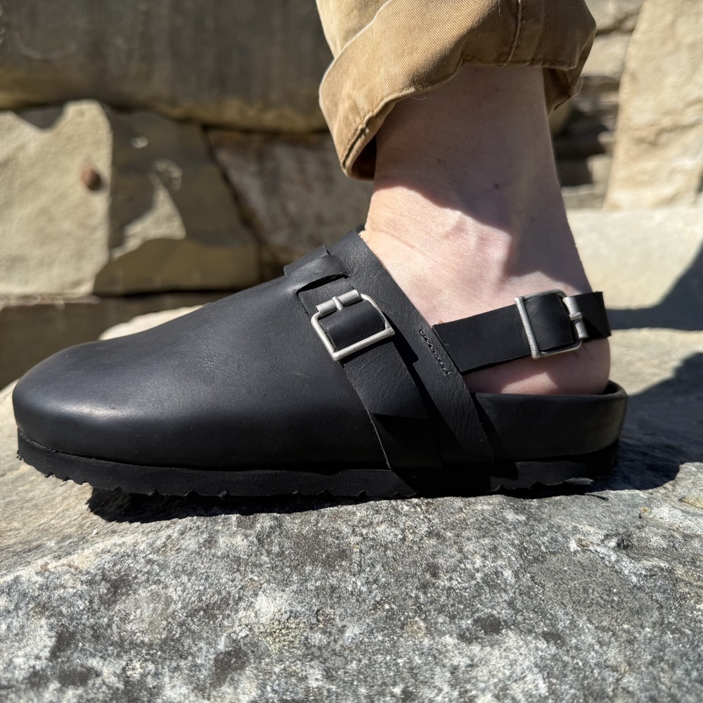 Black leather sandal worn with the slingback strap and buckle fastened around the ankle